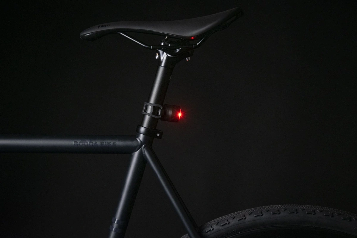 Booda Bike frame at night with a saddle and seat post, a Reflection Mini rear light on its silicone strap glowing red below the saddle
