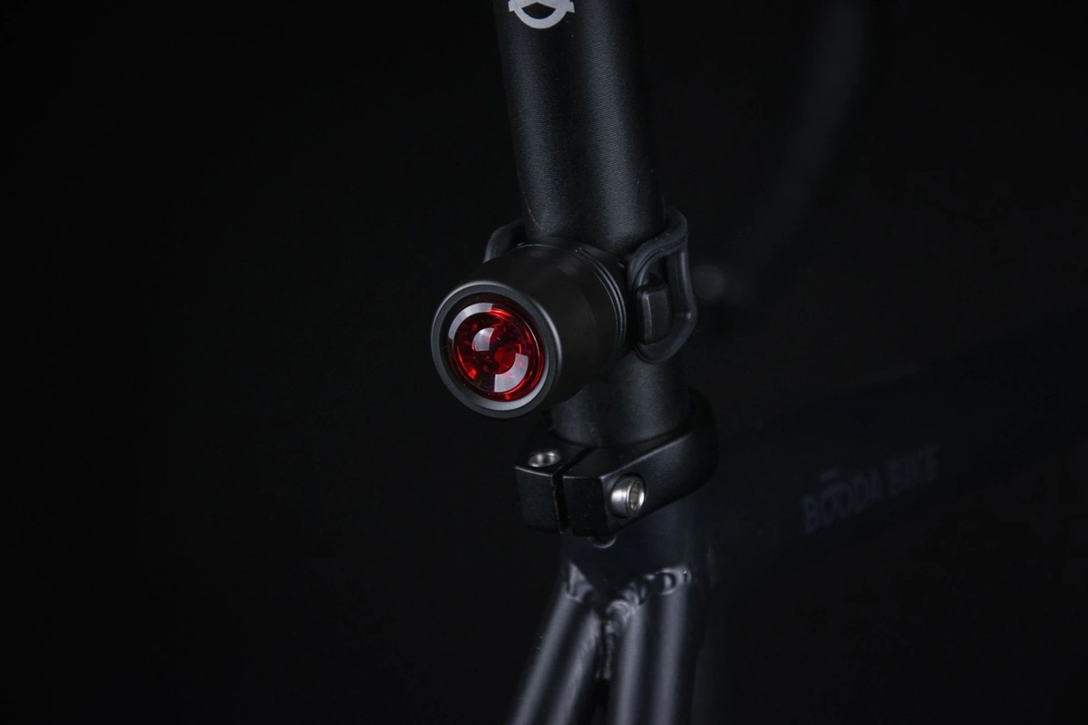 Close-up of the Reflection Mini rear light with its red lens on a black seat post just above the seat post clamp of a Booda Bike frame, in the dark