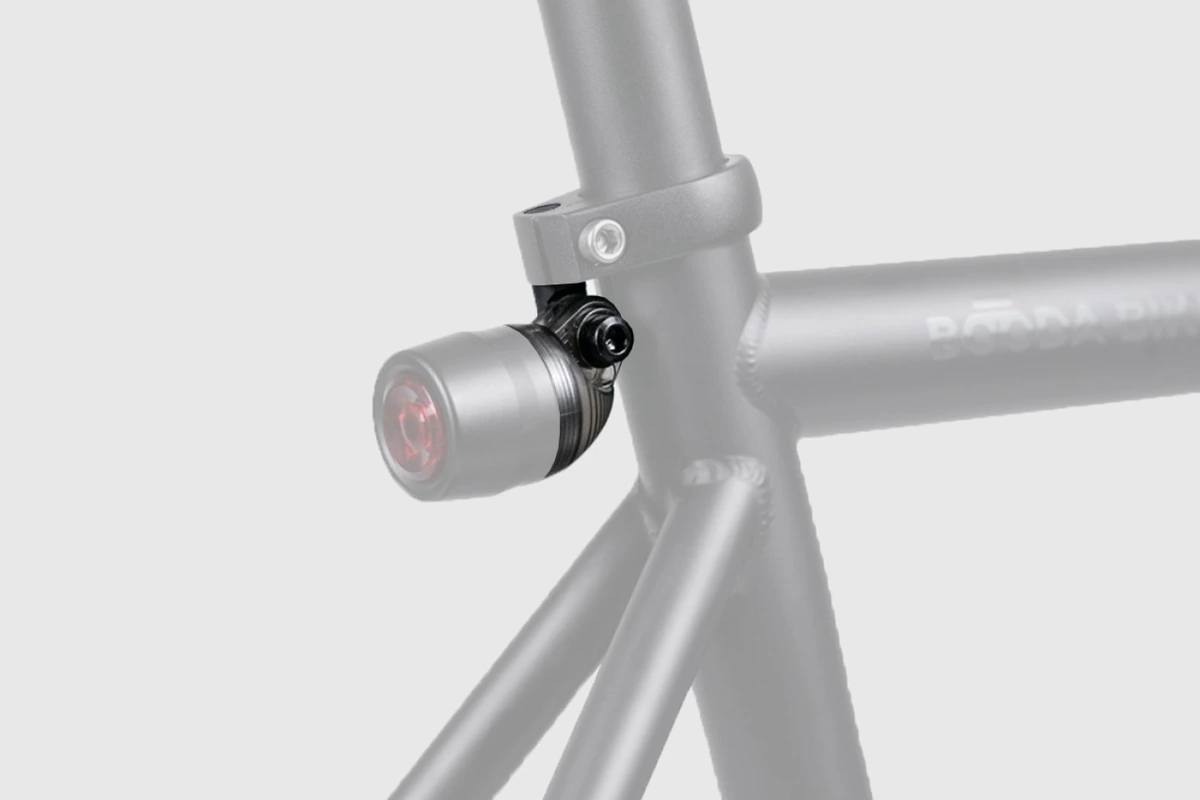 Illustration of a rear light with a red lens hanging from a bracket just below the seat post clamp of a faded grey Booda Bike frame