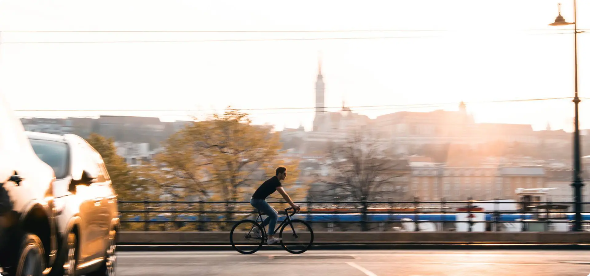 Booda Bike Astro, a single-speed commuter bike, in use: a rider on a city road at sunset with a car in the foreground