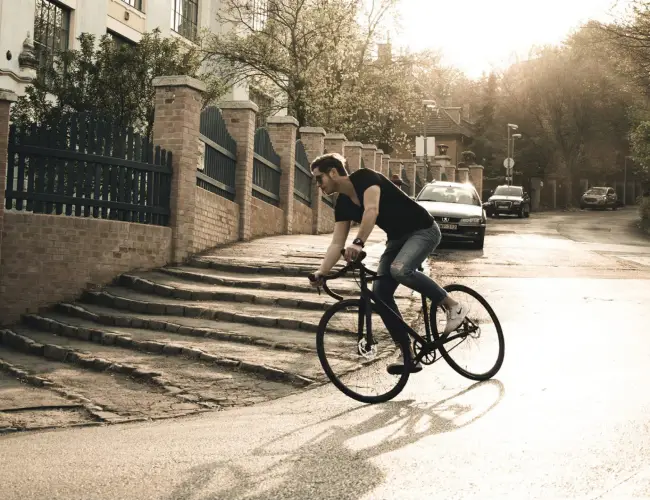 A cyclist rides a Booda Bike through a sunlit city street with stone steps