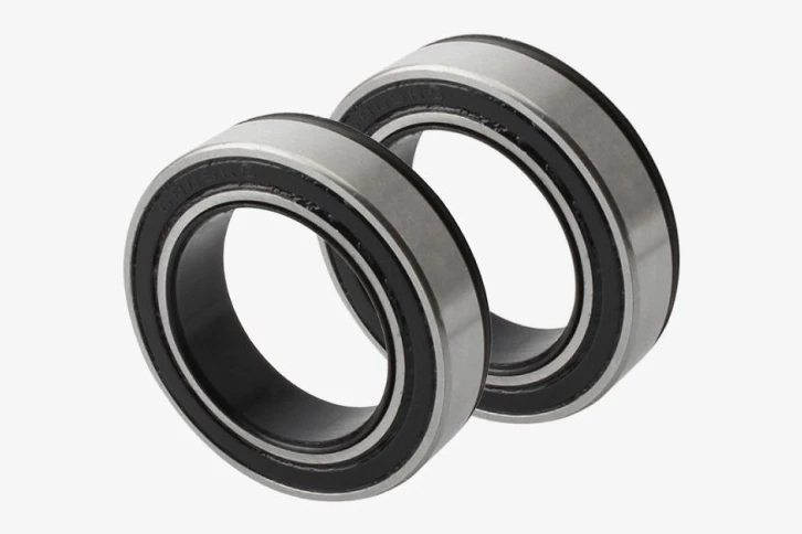 Two sealed bearings with black seals and silver rings leaning against each other on a light grey background