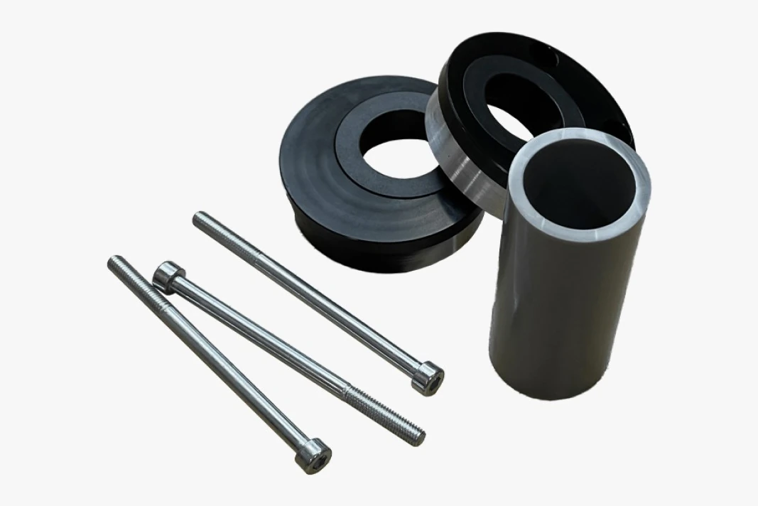 Black eccentric bottom bracket shells, a tube and three long socket-head bolts on a light grey background