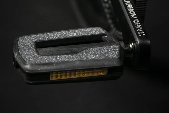 Black plastic flat pedal with a textured surface and an amber element on its edge, fitted to a crank arm with Carbon Drive lettering on a dark background
