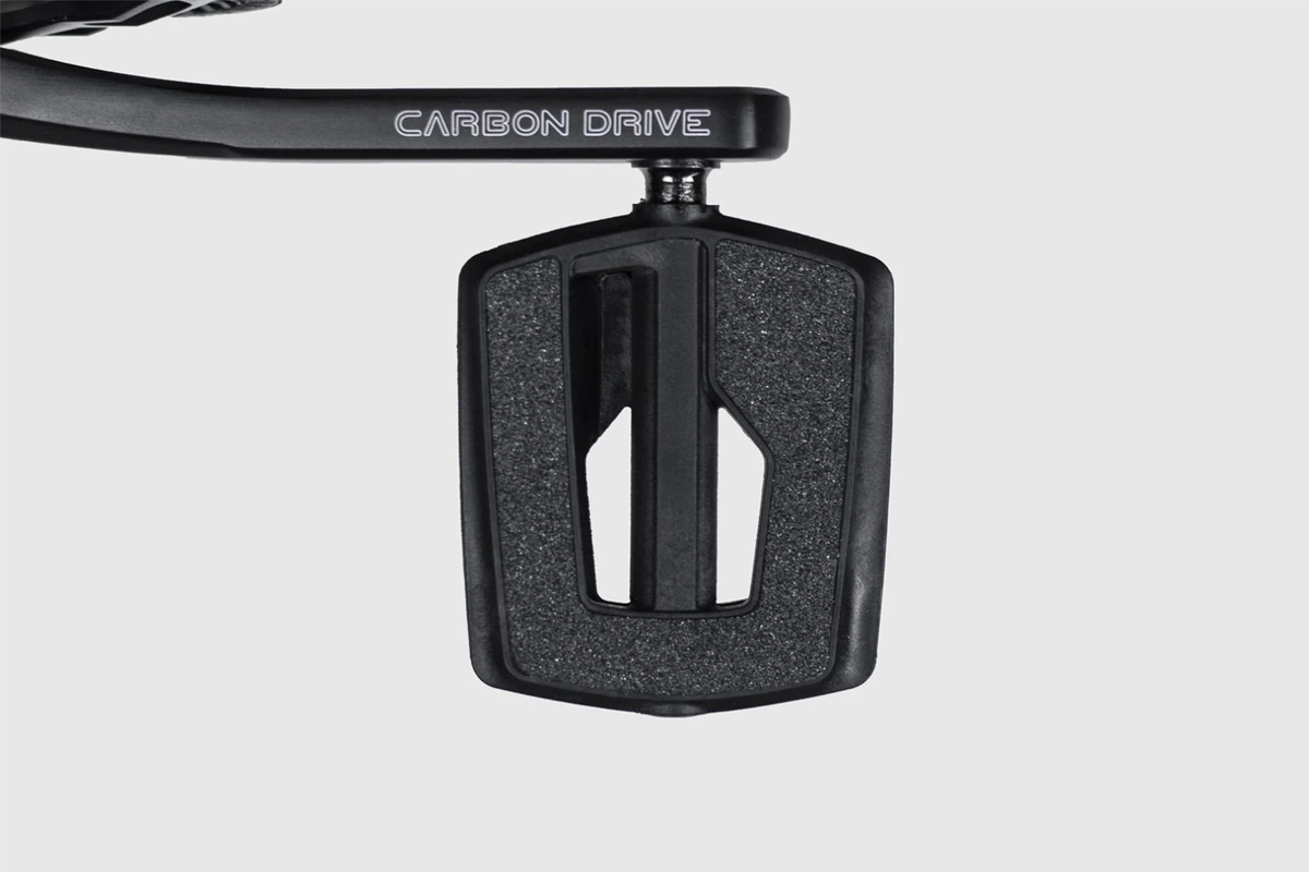 Black plastic flat pedal with a textured top surface at the end of a crank arm marked Carbon Drive, on a light grey background