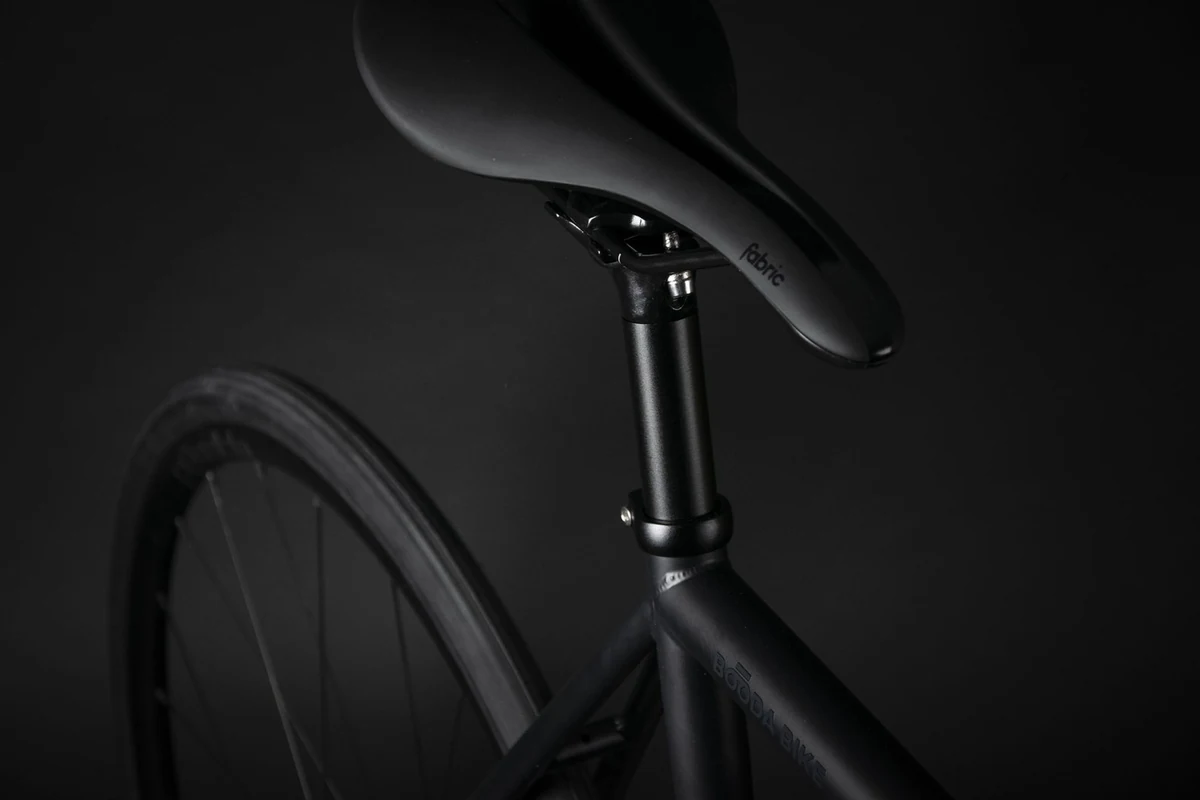 Saddle and seat post of a Booda Bike Pilot in a dark studio, with the rear wheel below
