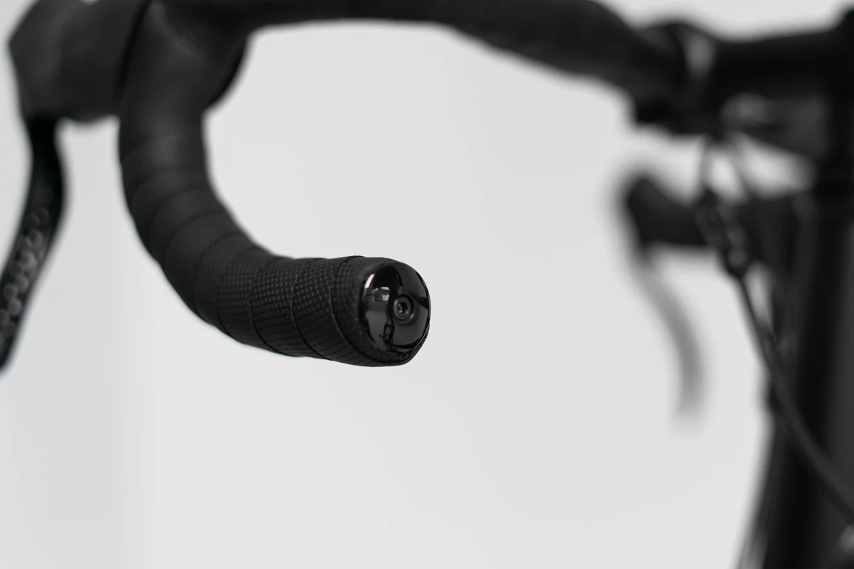 End of a drop handlebar wrapped in Multibender tape and closed with a black bar end plug, next to a brake lever