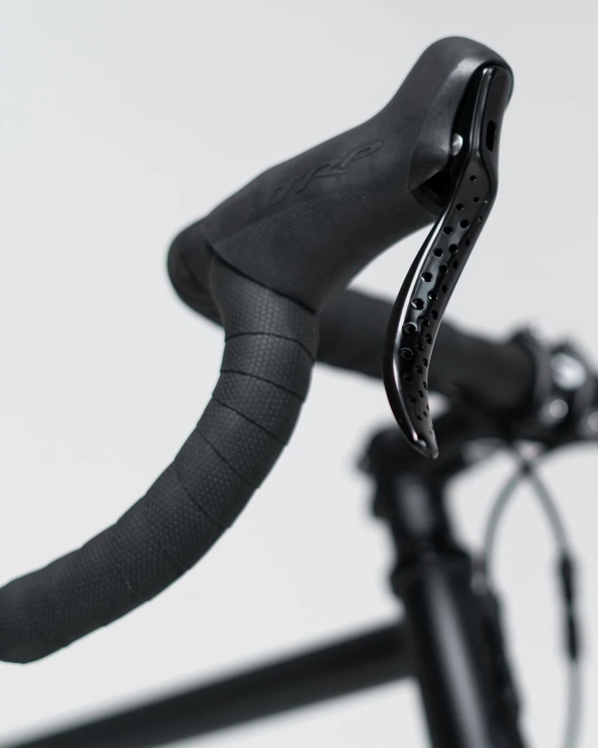 Black Multibender tape wrapped on the bend of a drop handlebar beside a perforated brake lever, on a light background