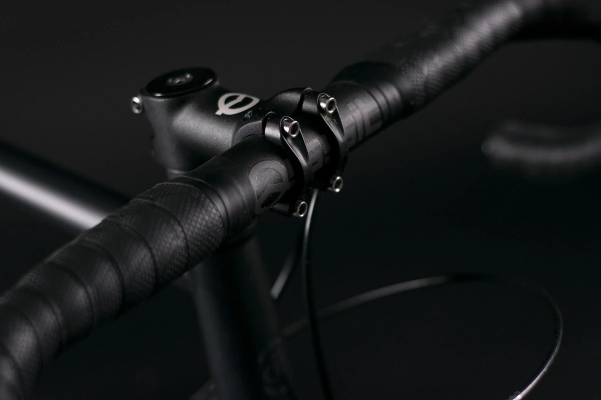 Dark close-up of a drop handlebar wrapped in black textured Multibender tape next to the stem, on a Booda Bike Hiker