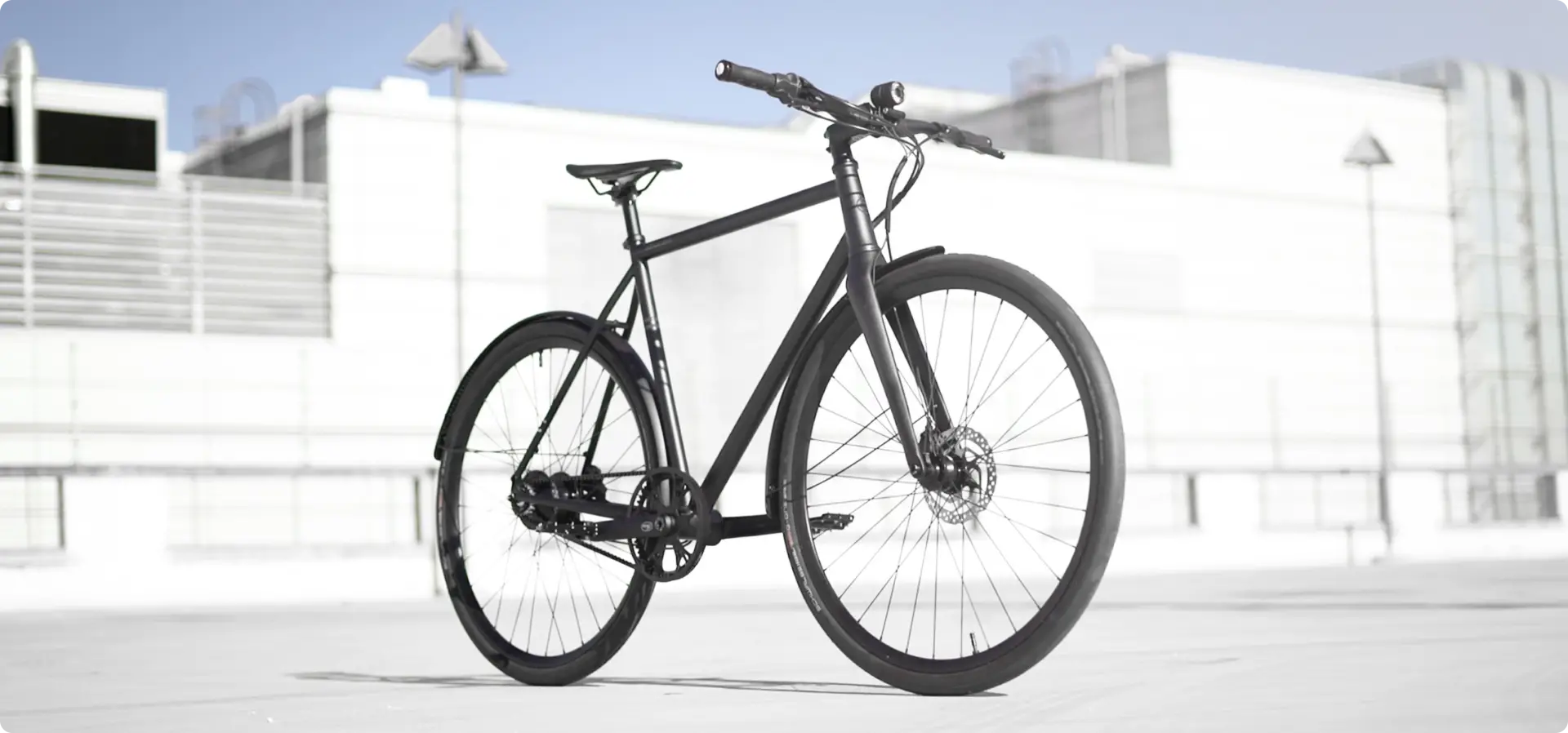 Booda Bike Pulse – Rohloff: fekete, szíjhajtású, agyváltós trekking kerékpár egy fehér épület előtt parkolva