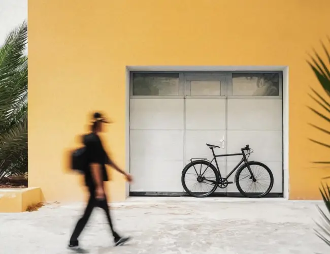 Egy járókelő elsétál a sárga fal és egy garázskapu előtt parkoló Booda Bike mellett