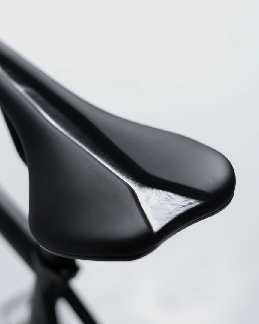Black saddle on a seat post with a blurred bicycle frame behind it