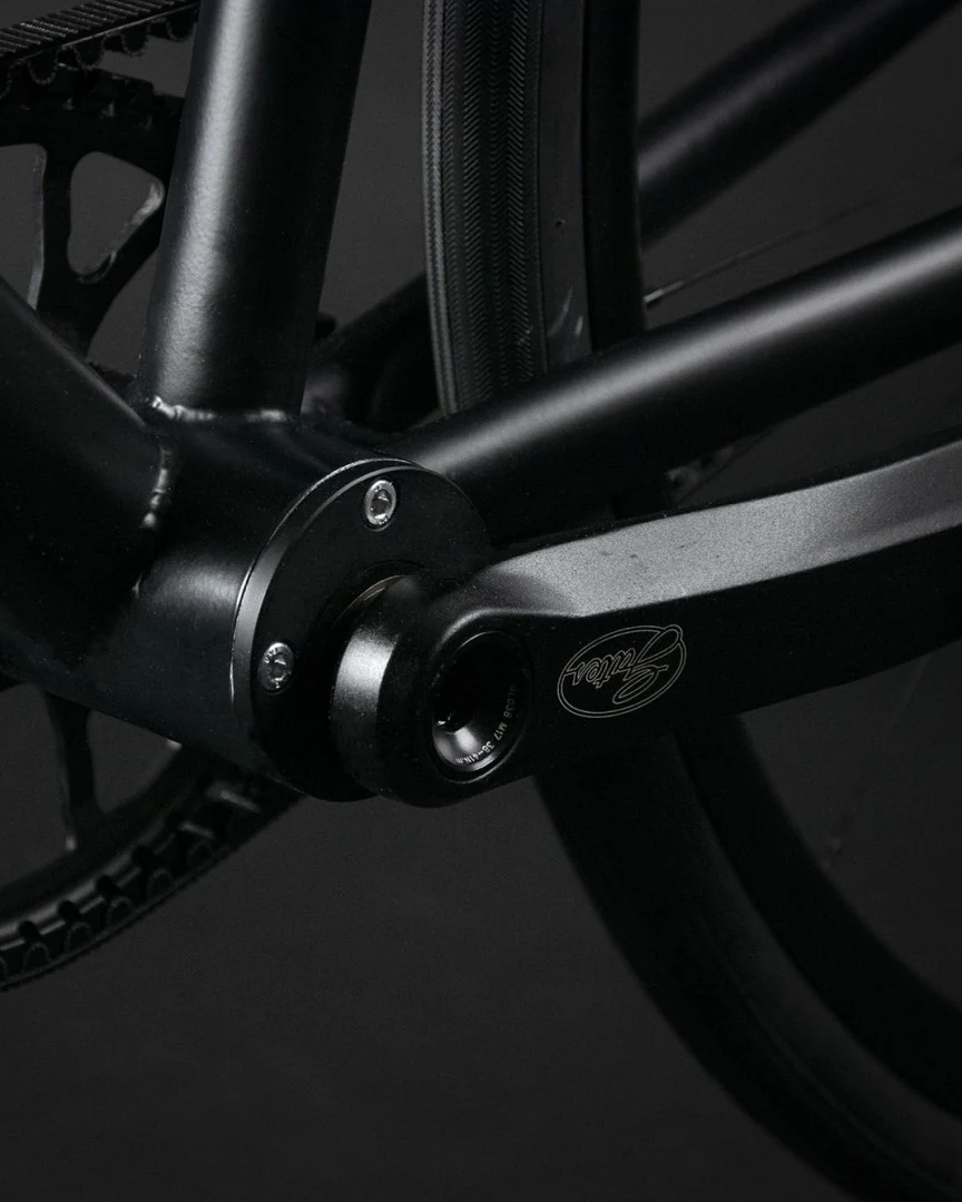 Eccentric bottom bracket shell with cap bolts and the crank axle on a Booda Bike frame in a dark studio