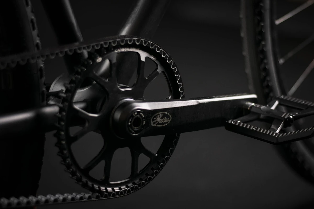 Dark close-up of a belt-drive sprocket and crank arm with a Sport Pedal Alu fitted, on a Booda Bike Hiker