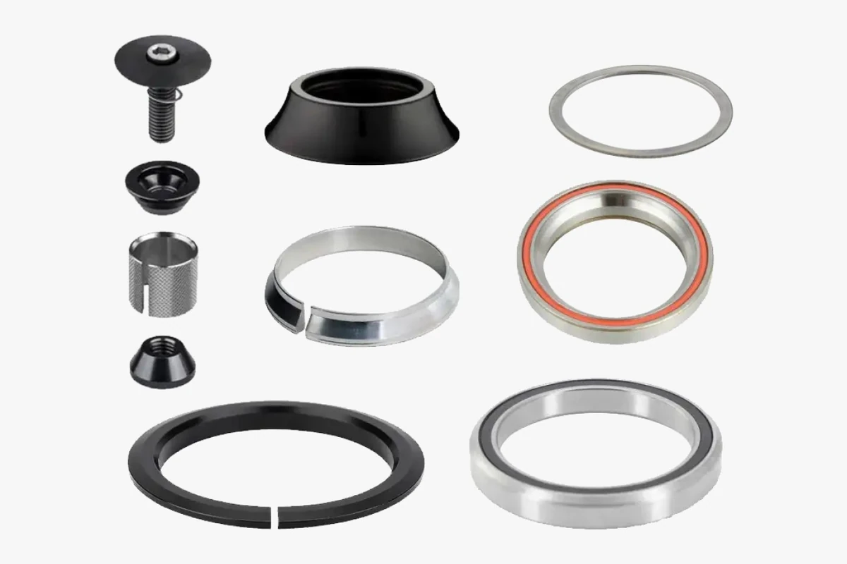 Headset kit parts laid out on a light grey background: two bearings with orange and black seals, flat and tapered rings, a black dust cap, a knurled expander sleeve with its cone, and a bolt with a top cap