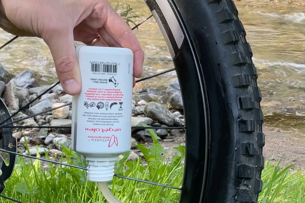 Effetto Mariposa Végétalex 250 ml Flasche mit Einspritzschlauch beim Befüllen eines Mountainbike-Reifens durch das Ventil, im Freien