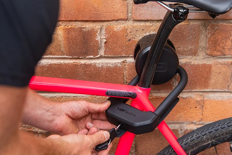 Man locking a road bike to a Hiplok ANKR wall anchor with a key