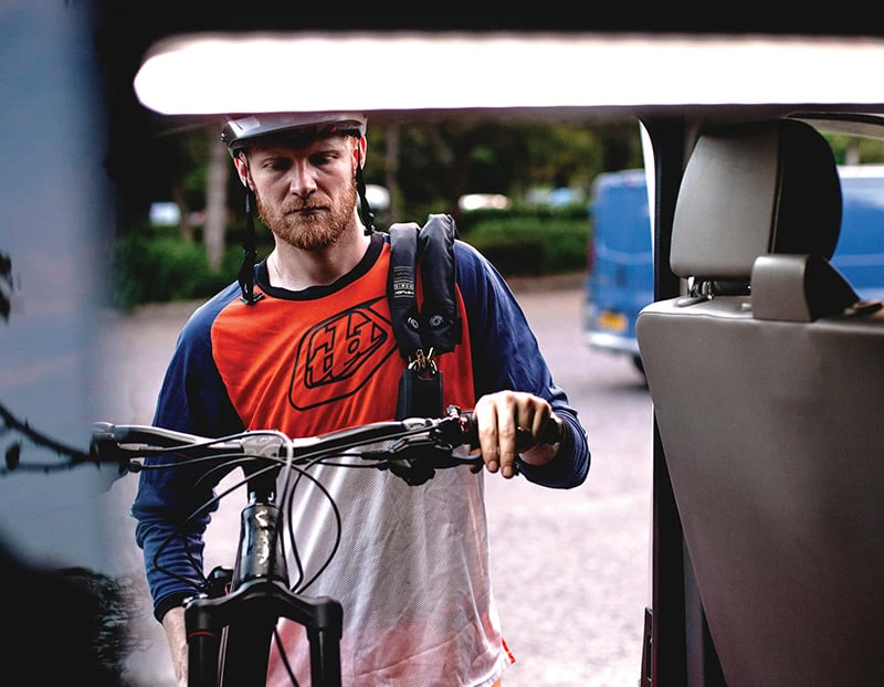 Man loading a mountain bike into a van with the Hiplok HOME GOLD chain over his shoulder