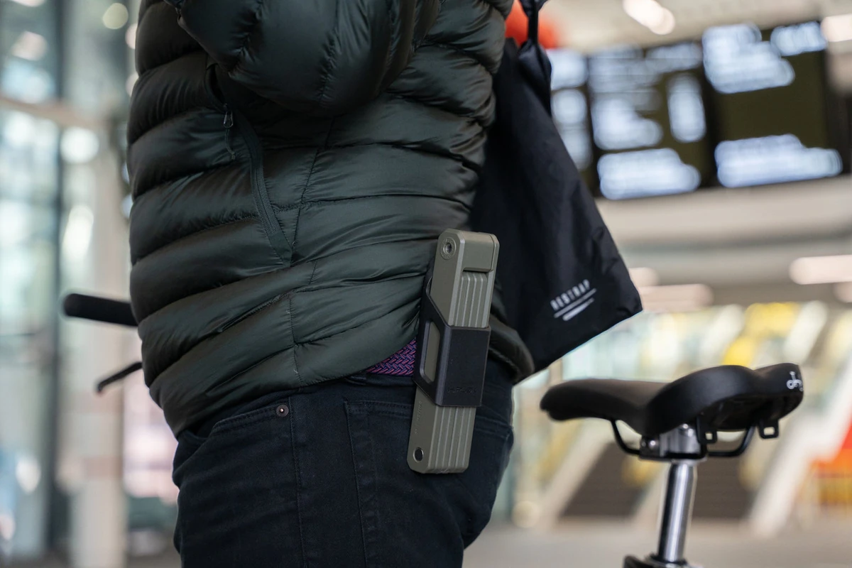 Hiplok SWITCH folding lock clipped to a rider's belt next to a folding bike