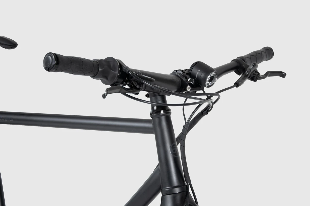 Booda Bike Pulse cockpit seen from the side: Noirette handlebar with grips, brake levers and a headlight above the stem, with the steel top tube behind it
