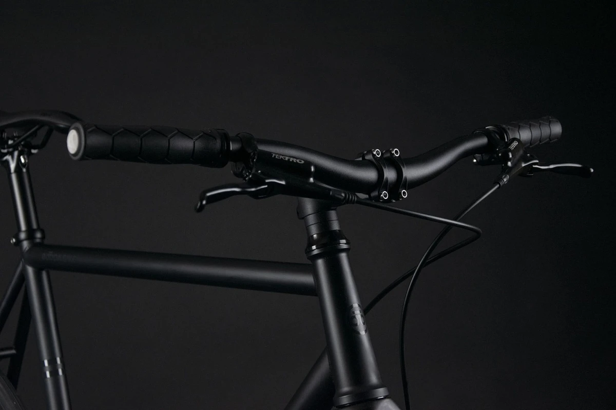 Booda Bike Pilot cockpit from the side in a dark studio: black riser handlebar with grips, brake levers and the stem above the top tube