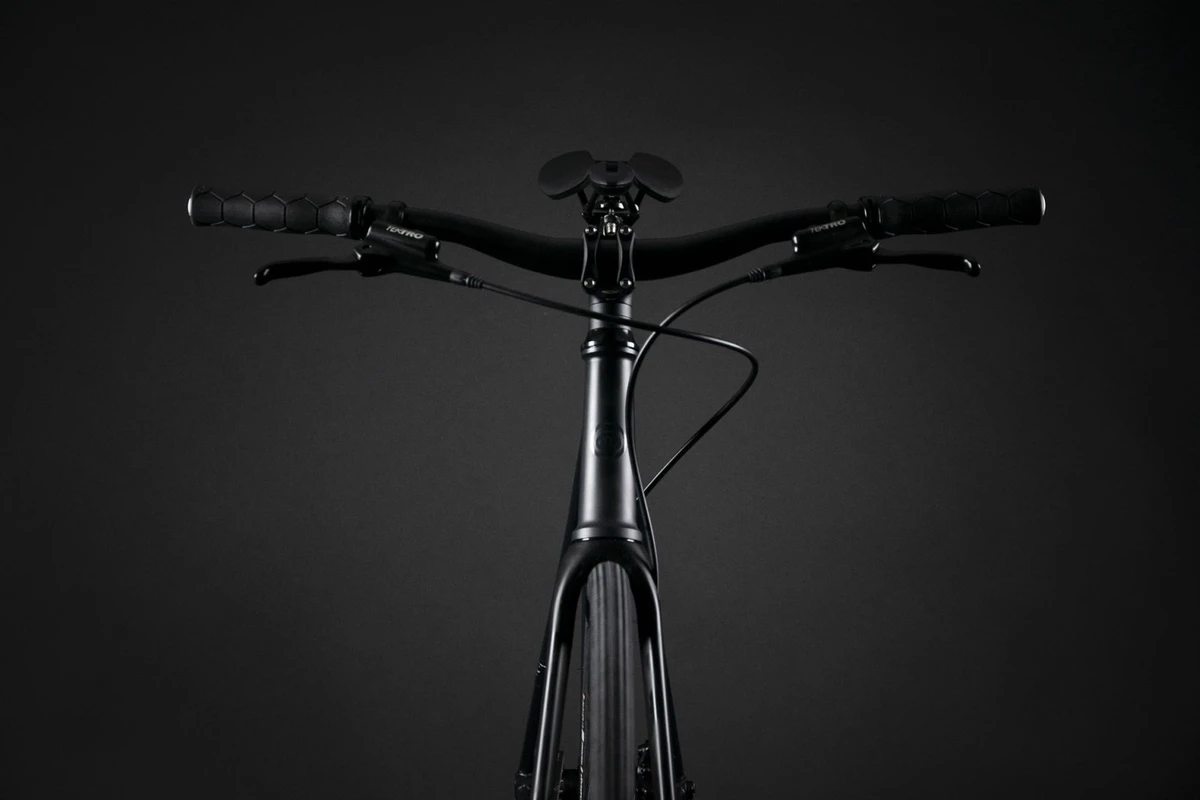 Booda Bike Pilot photographed from the front in a dark studio: riser handlebar with grips and brake levers above the stem and head tube