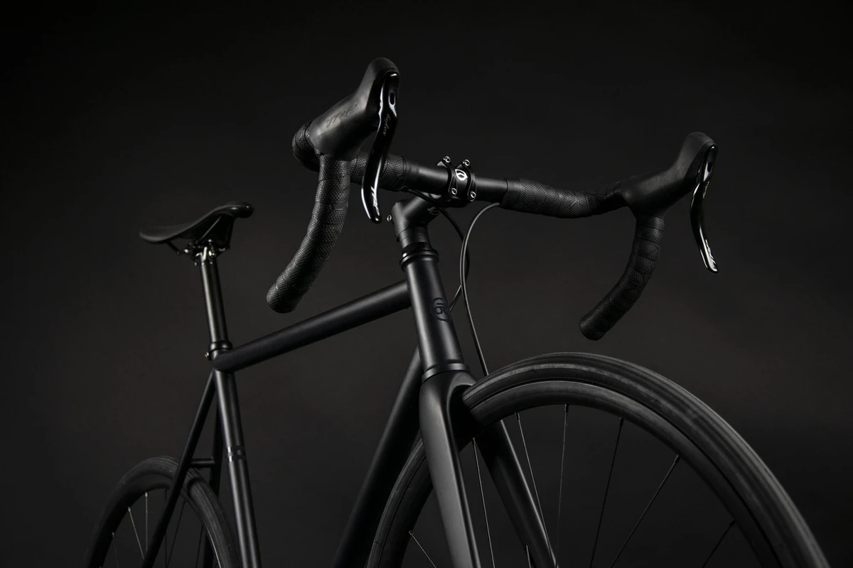 Booda Bike Astro photographed from the front left in a dark studio, showing its aluminium drop handlebar with bar tape and brake levers above the stem