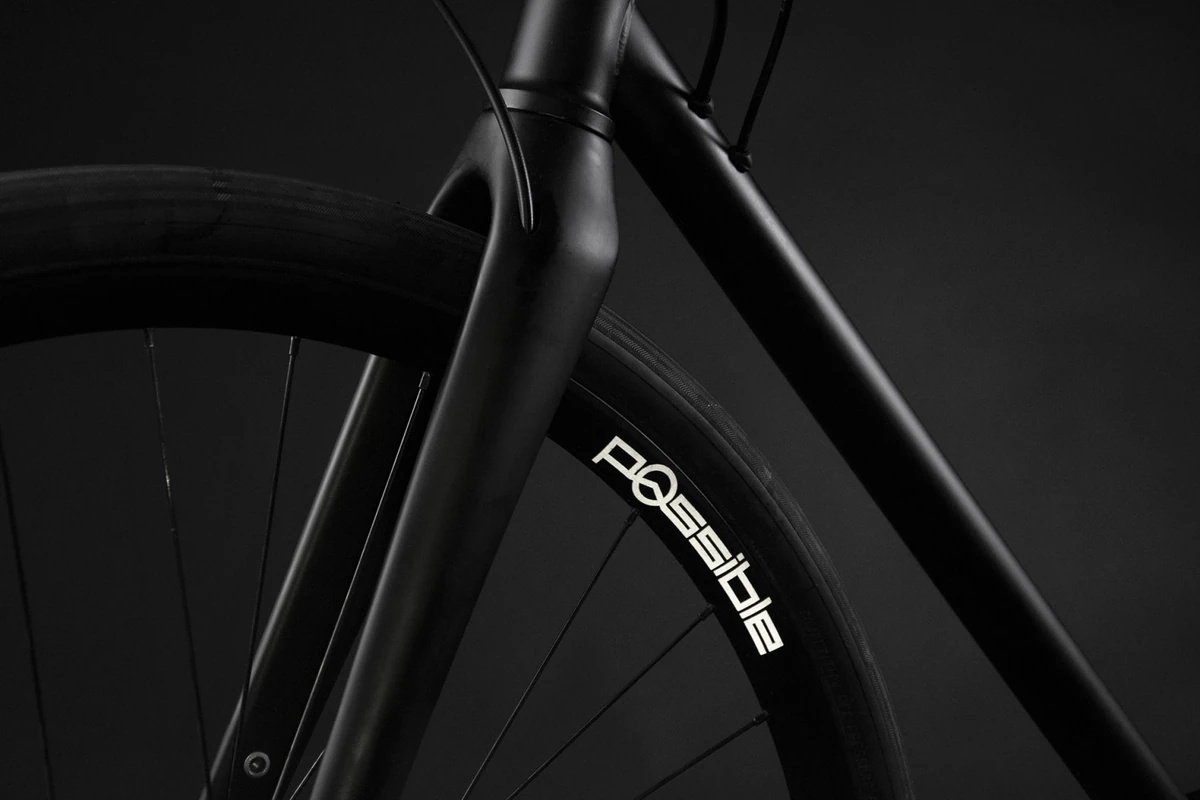 Dark close-up of a black bicycle: the carbon fork crown and head tube above a front wheel with a Possible rim label