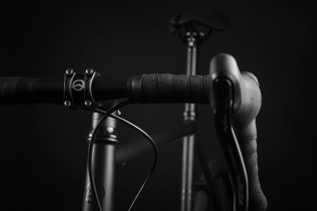 Black four-bolt stem with a white outlined logo on a taped handlebar, a brake lever in the foreground and the saddle blurred behind, on the Booda Bike Astro