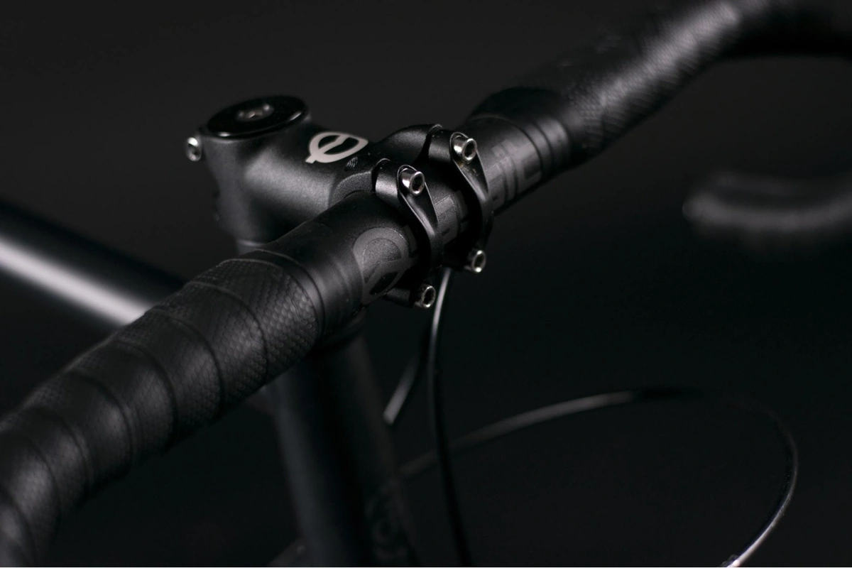 Close-up of a black stem with a white logo clamping a black bar-taped drop handlebar on the Booda Bike Hiker