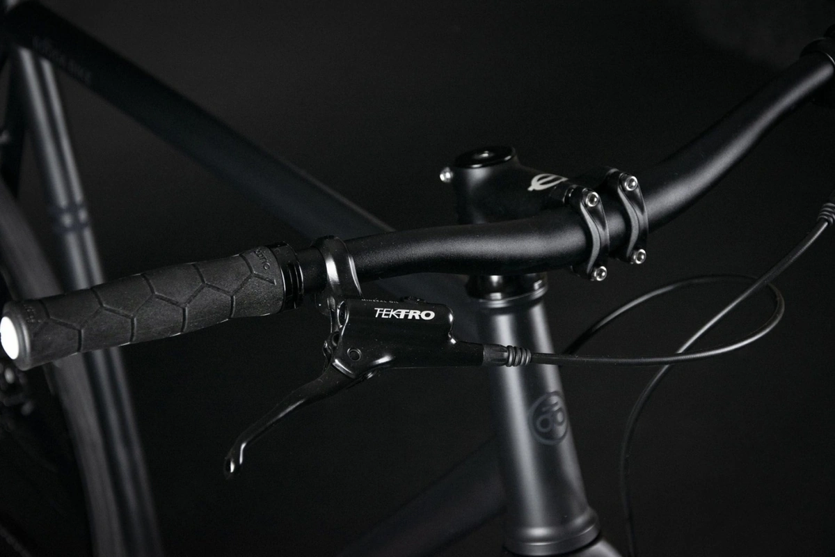 Flat handlebar with a ribbed black grip, a Tektro brake lever and a black four-bolt stem with a white logo on the Booda Bike Pilot