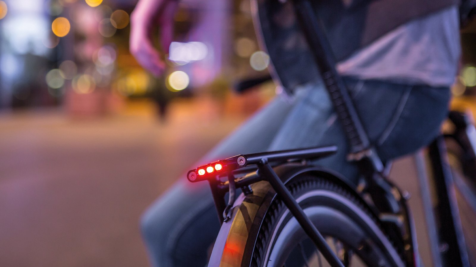 Supernova E3 Tail Light 2 pirosan világít egy éjszaka a városban közlekedő kerékpár hátsó csomagtartóján